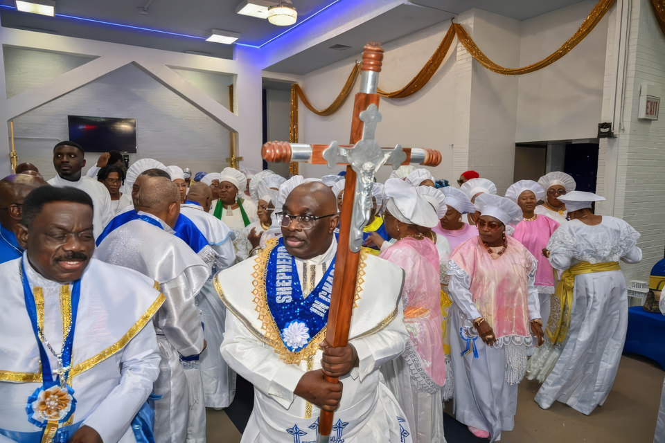 The Harvest of Prosperity procession enters the sanctuary, led by a processional cross, with women in white and pink garments following.