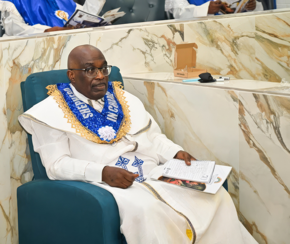 The Shepherd in Charge, wearing a blue Shepherd in Charge sash, seated in the sanctuary with a service programme.