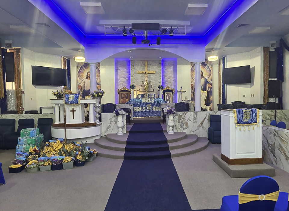 A wide view of the SBJ Luli Cathedral sanctuary, with rows of blue and gold chairs on either side of the aisle and the altar at the far end.